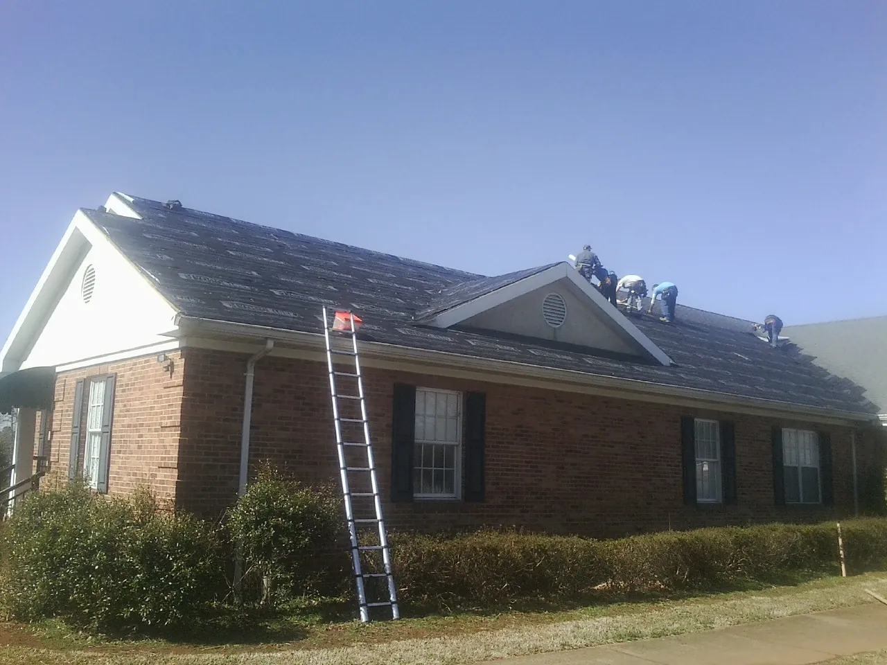 Crew tearing shingles off a brick ranch roof with a ladder set — Metal Roof Repair work by our crew in Cascade